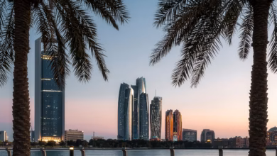 Abu Dhabi Corniche waterfront with calm beach, palm-lined promenade, and modern city skyline along the Arabian Gulf.