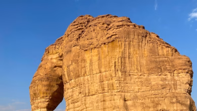 AlUla sandstone mountains rising above a vast Saudi desert landscape with dramatic rock formations and clear blue sky