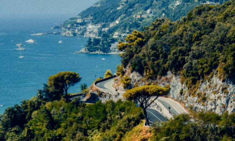 Amalfi Coast road view with winding coastal cliffs, pastel hillside villages, and sparkling Mediterranean sea under a clear s