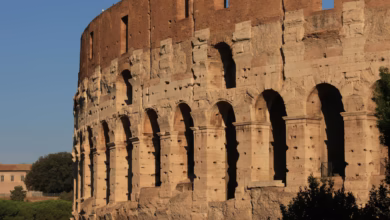 Ancient Rome architecture with weathered stone columns, crumbling Roman ruins, and historic arches set against a clear sky in
