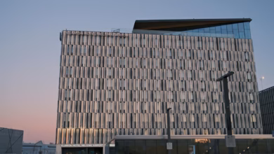 Modern airport hotel exterior at dusk with illuminated windows, nearby runway lights, and a sleek city skyline in the backgro
