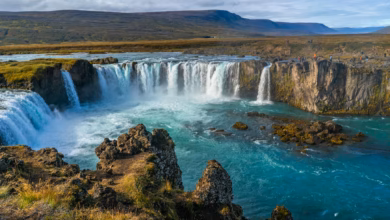 Dramatic Iceland waterfall cascading over dark volcanic cliffs, surrounded by lush green moss and rugged scenic landscape.