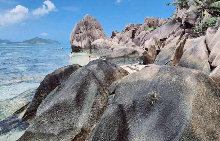 Seychelles luxury island tropical beach with granite rocks, turquoise water, and lush palm-fringed shoreline at sunset.