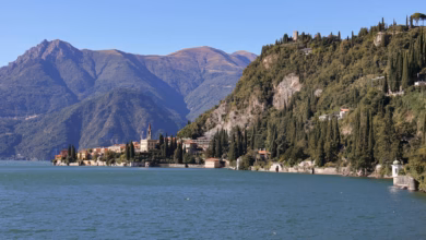 Scenic Italian lake with clear blue water, mountain backdrop, and charming lakeside town architecture in summer, Italy lakes