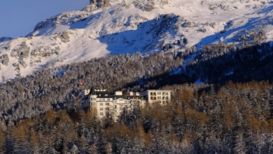 Elegant Switzerland luxury hotel overlooking snow-capped Alpine peaks and a serene mountain valley, with a stunning lakeside