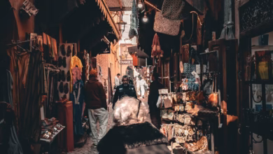 Narrow Marrakesh souk alley with traditional Moroccan architecture, colorful market textiles, and hanging lanterns in warm ea
