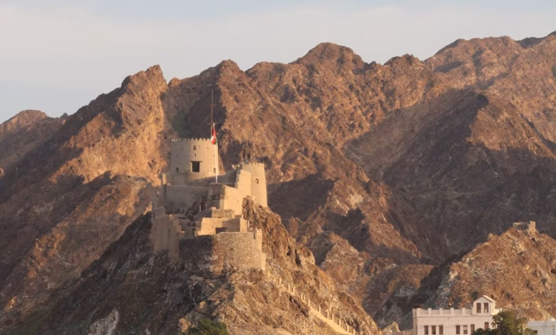 Panoramic Muscat Oman coastline with historic forts, traditional Omani architecture, and rugged mountains beside the sea.