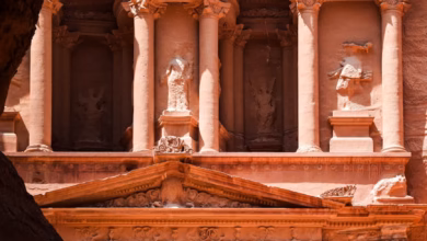 Ancient Petra Jordan treasury facade carved into rose-colored sandstone cliffs, with dramatic archaeological ruins and desert