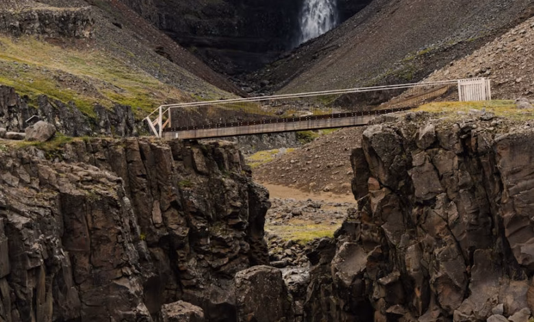 Iceland waterfall cascading beside dramatic volcanic cliffs in a scenic nature view with rugged rock formations and lush gree