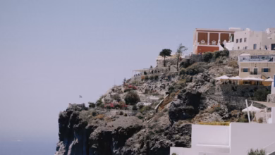 Whitewashed cliffside buildings with blue domes overlooking the caldera in Santorini, Greece, with the Aegean Sea and volcani