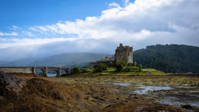 Scenic Scotland castle landscape with a historic stone fortress beside misty lochs, rolling green hills, and dramatic country