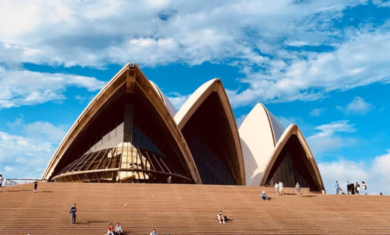 Sydney Opera House exterior with iconic white sail-shaped shells on Sydney Harbour, framed by waterfront skyline and blue wat