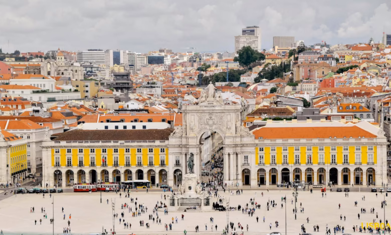 Colorful Lisbon hillside cityscape with historic terracotta rooftops, pastel buildings, and the Tagus River in the distance,